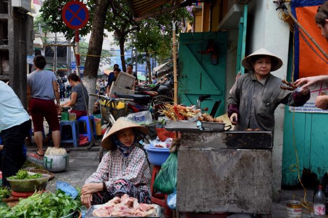 Street food vendor preparing a pork skewer